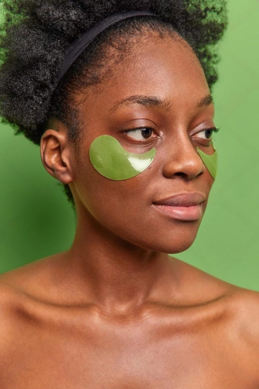 Woman applying green hydrogel under-eye patches to treat dark circles